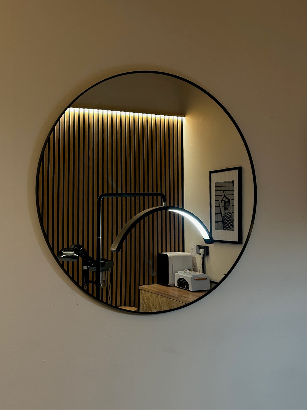 A round mirror reflecting the wood-slat treatment-room wall at SHY